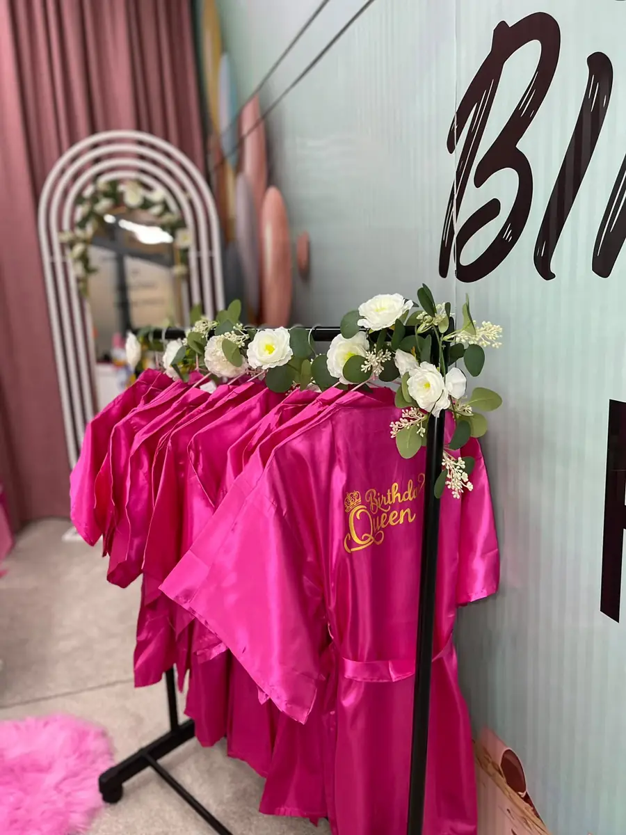 Pink robes printed Birthday Queen, hanging under white flowers