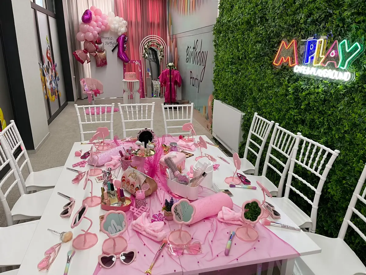 The long pink table set with mirrors, brushes and heart sunglasses in front of the plant wall
